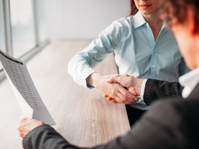 Unrecognizable businesswoman holding document and shaking hand of business partner after signing of contract. They sitting at table. Negotiation concept